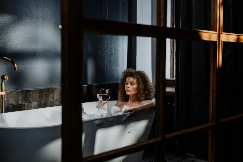 a woman with red hair is sitting in a bathtub holding a glass of wine