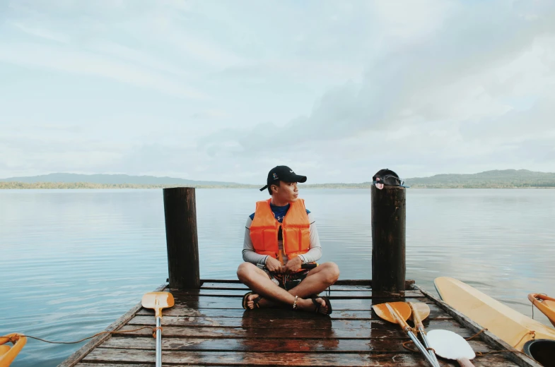 a man sitting on the end of a dock next to some paddle boats