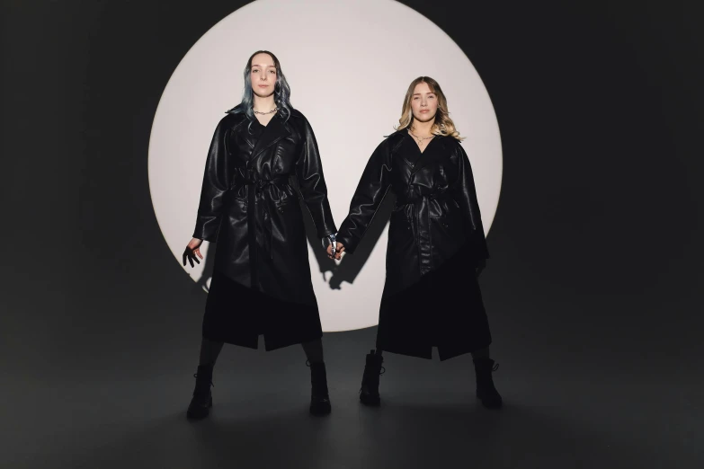 two people in black coats standing on the same dark background