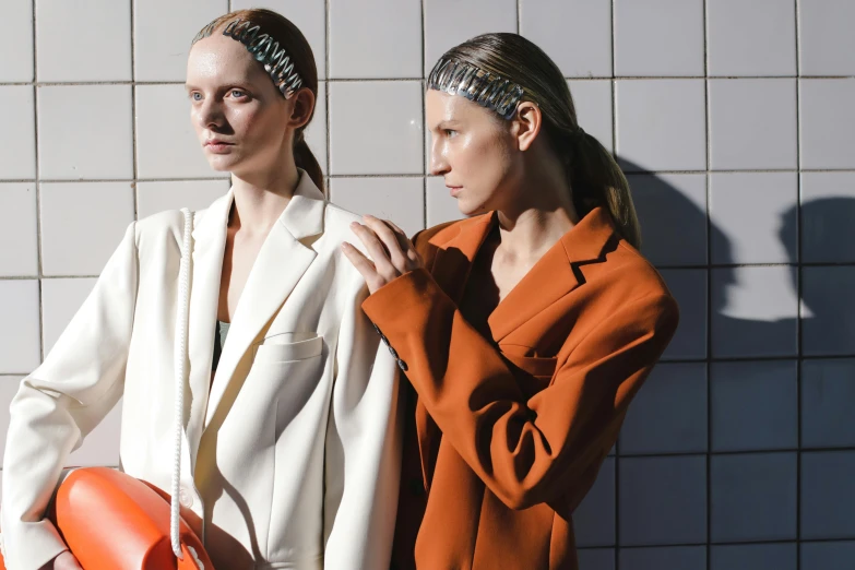 two women wearing orange and white outfits one holding an orange umbrella