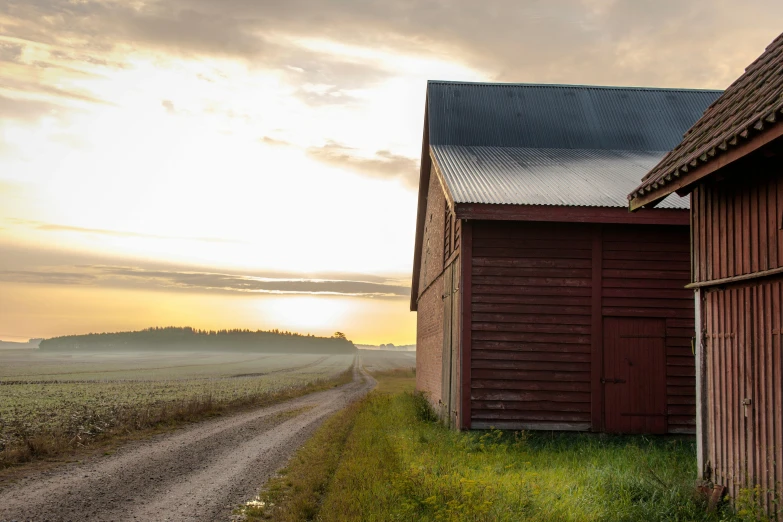 the sun is setting behind some red barns