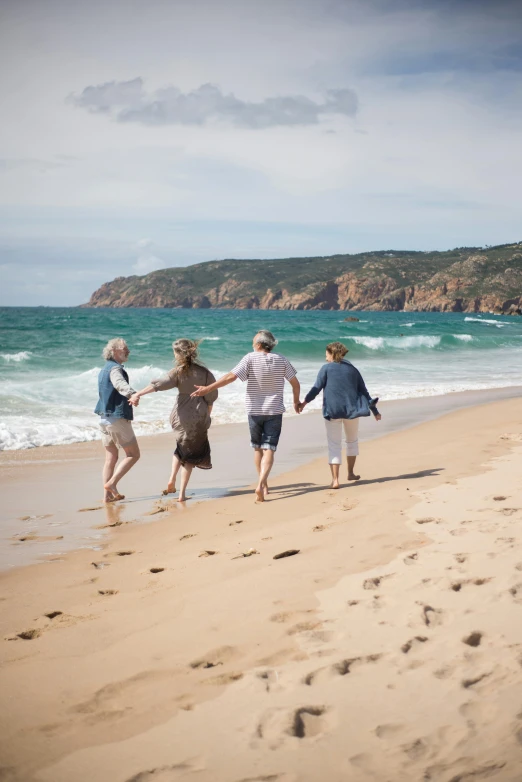 four people are holding hands while walking on the beach