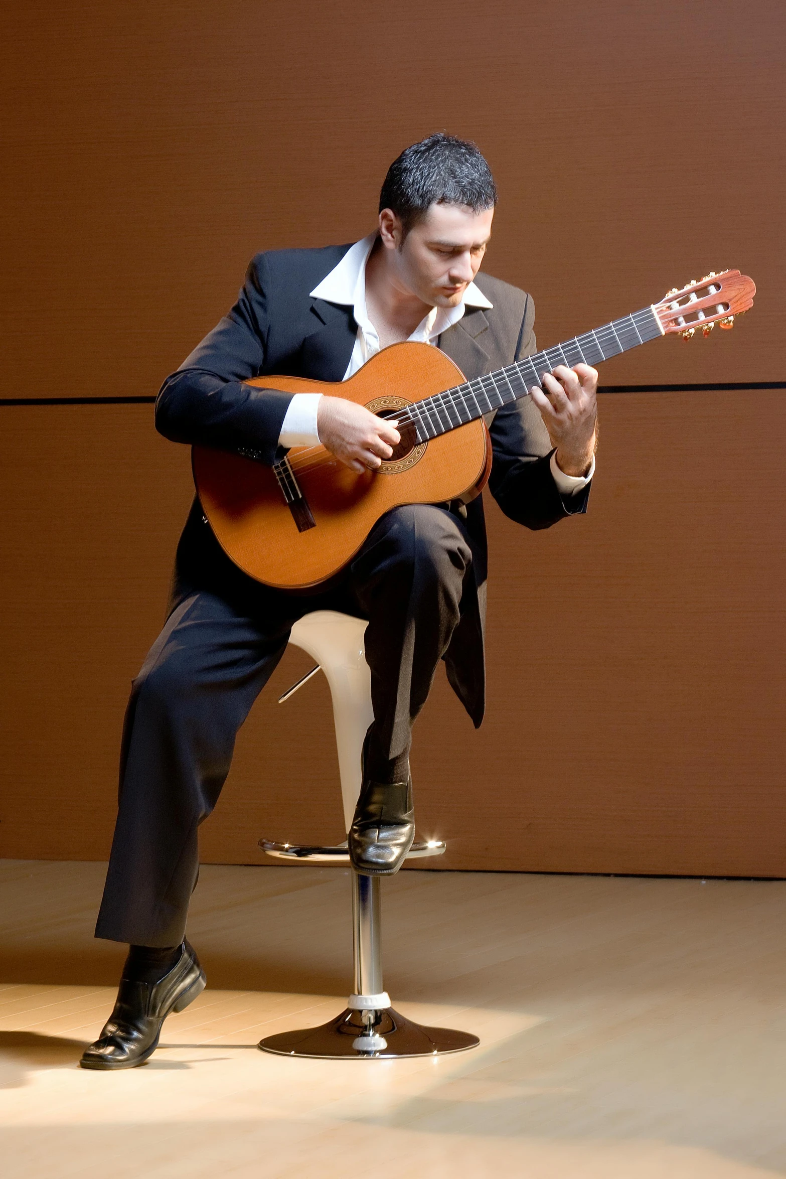 man sitting on chair playing an acoustic guitar
