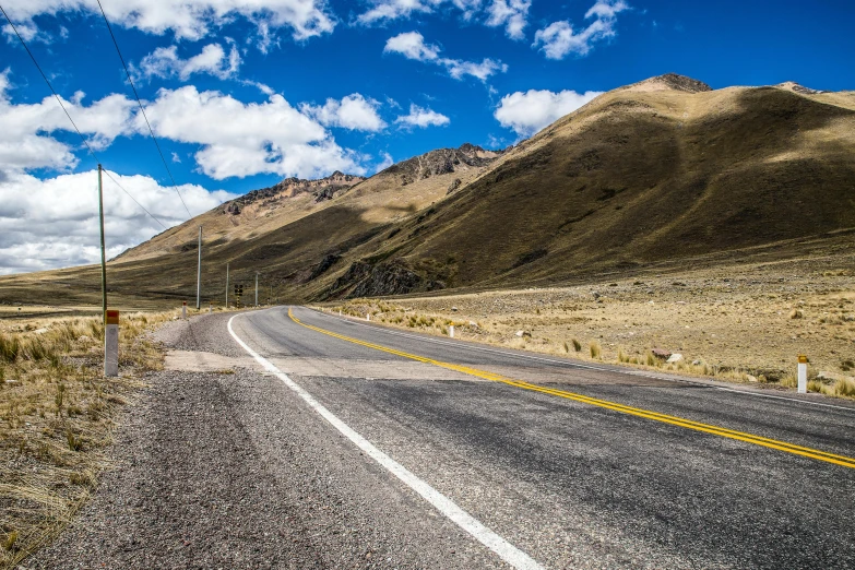 a lonely road going past an arid hill