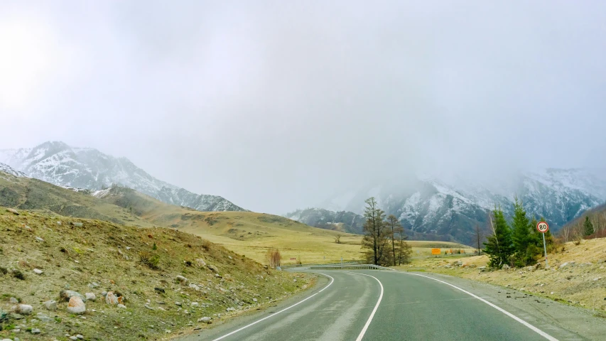 a single stretch of road with snow capped mountains in the distance