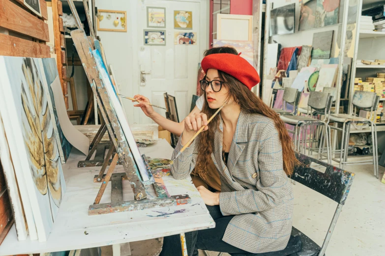a woman sits at a table in front of an easel while holding her brush
