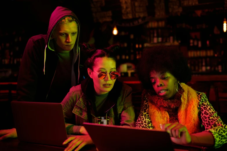 three people looking at a laptop in a bar