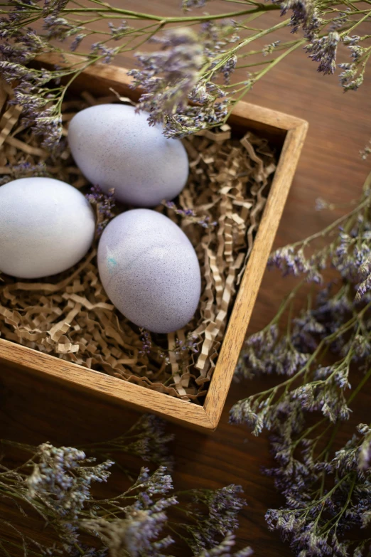 three eggs sitting in a wooden crate next to lavender flowers