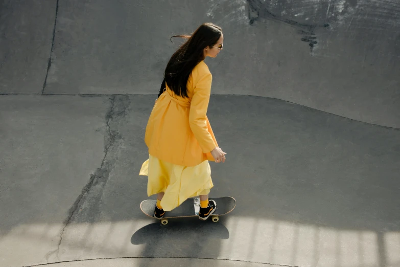 a girl in yellow is walking on the sidewalk with her skateboard