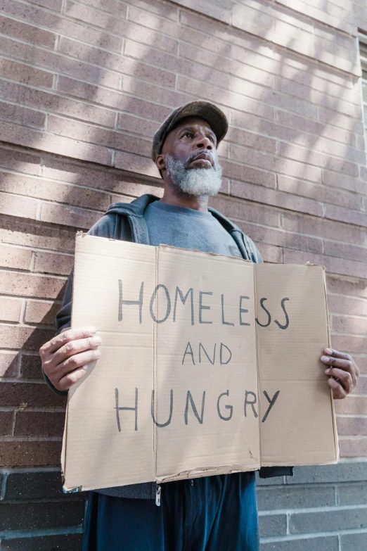 a man standing with a cardboard sign that says homeless and hungry