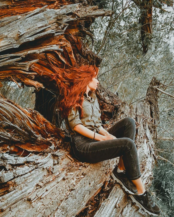 the young red headed woman is sitting on top of an old tree