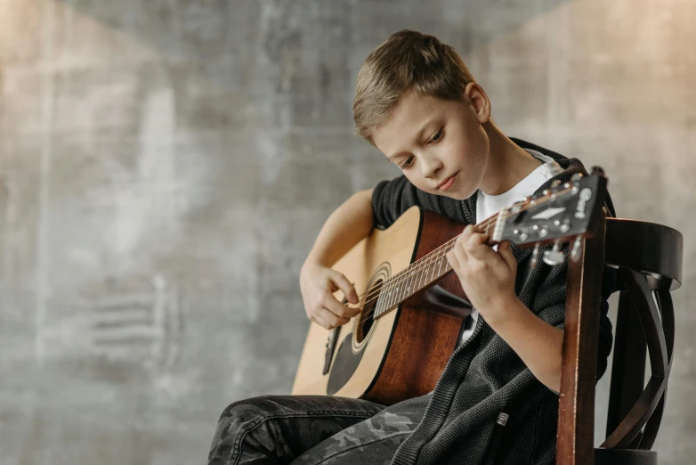 a boy holding a guitar while sitting down