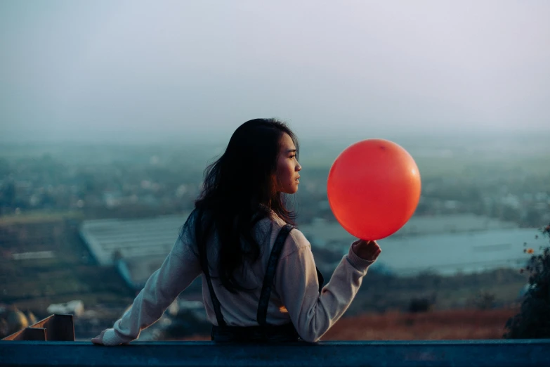 the girl holds a red balloon on top of a roof