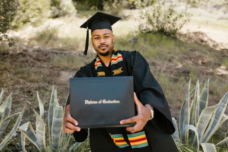 the graduate poses in a graduation gown holding his certificate