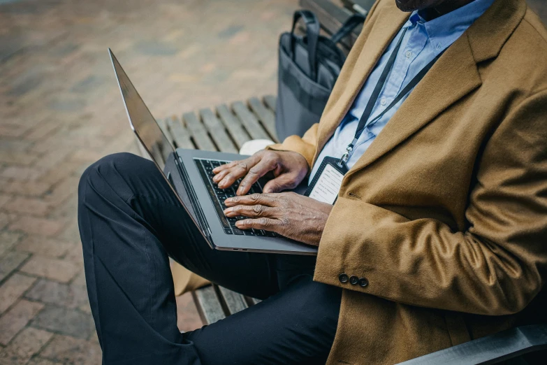 a man sitting on a park bench using his laptop