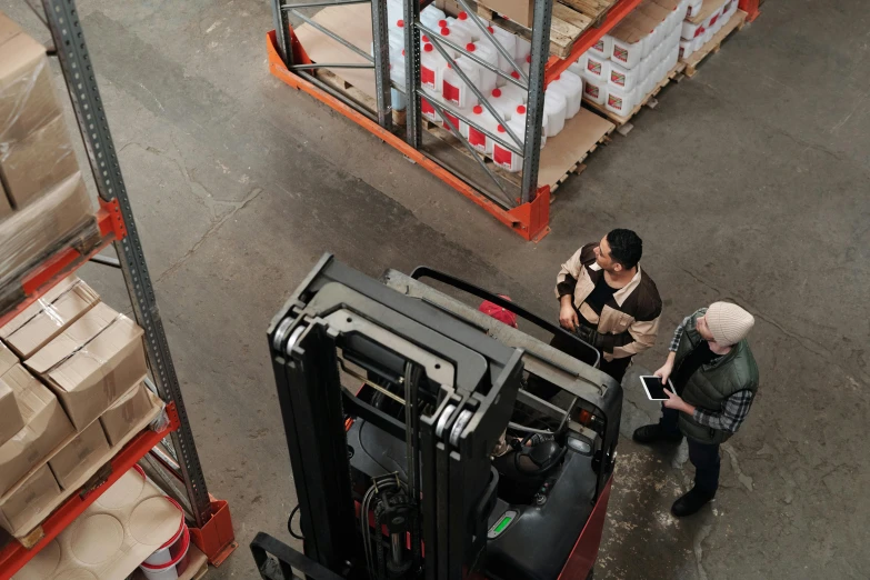 two women standing next to a forklift with many goods