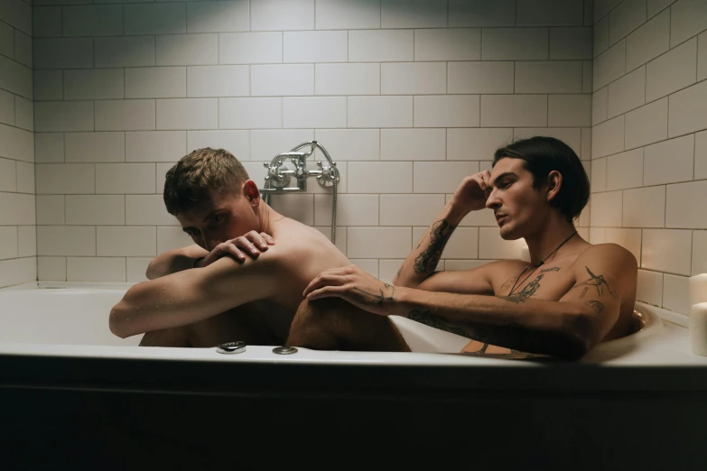 two men laying in a bathtub with one resting his arm on another man's chest