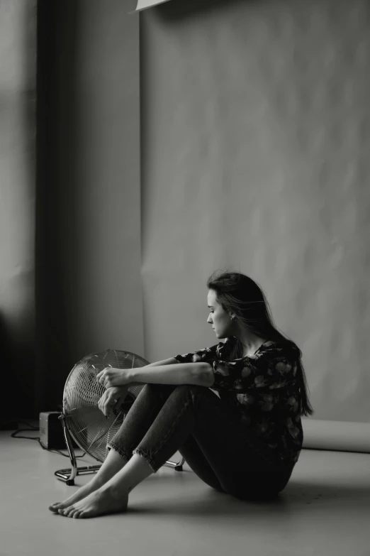 a woman sitting on the floor next to a fan