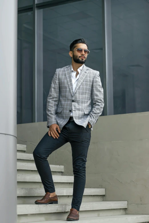 a man in a plaid blazer poses on some stairs