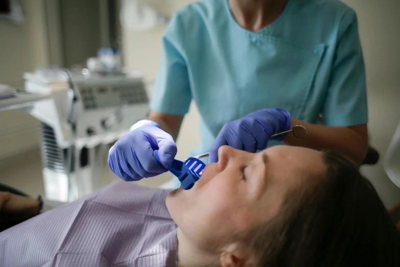 woman in scrubs getting her teeth brushed by a dental care professional