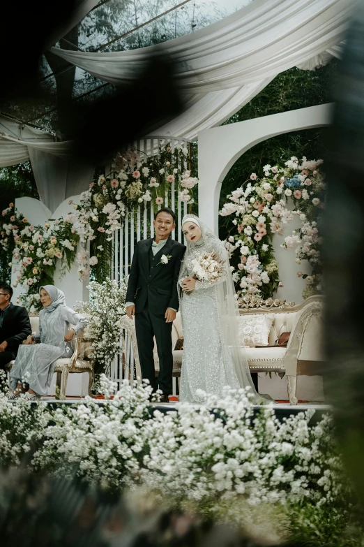 a man and a woman in a white gown under an arch with flowers