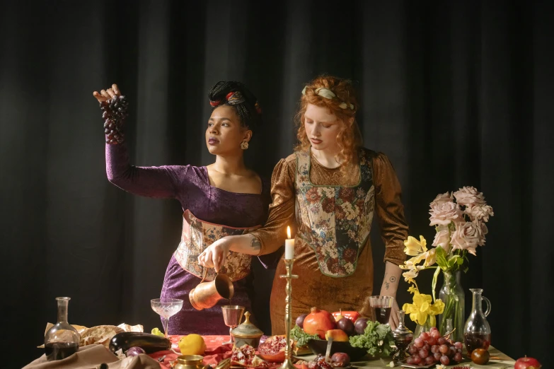 two women dressed in renaissance costume preparing a table