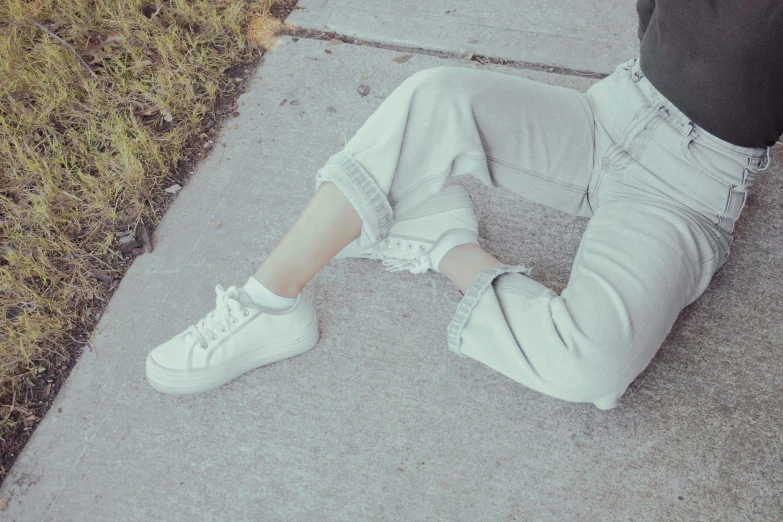 a woman is laying on the sidewalk wearing ripped jeans and white sneakers