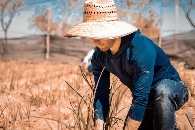 a man kneeling in a field wearing a straw hat