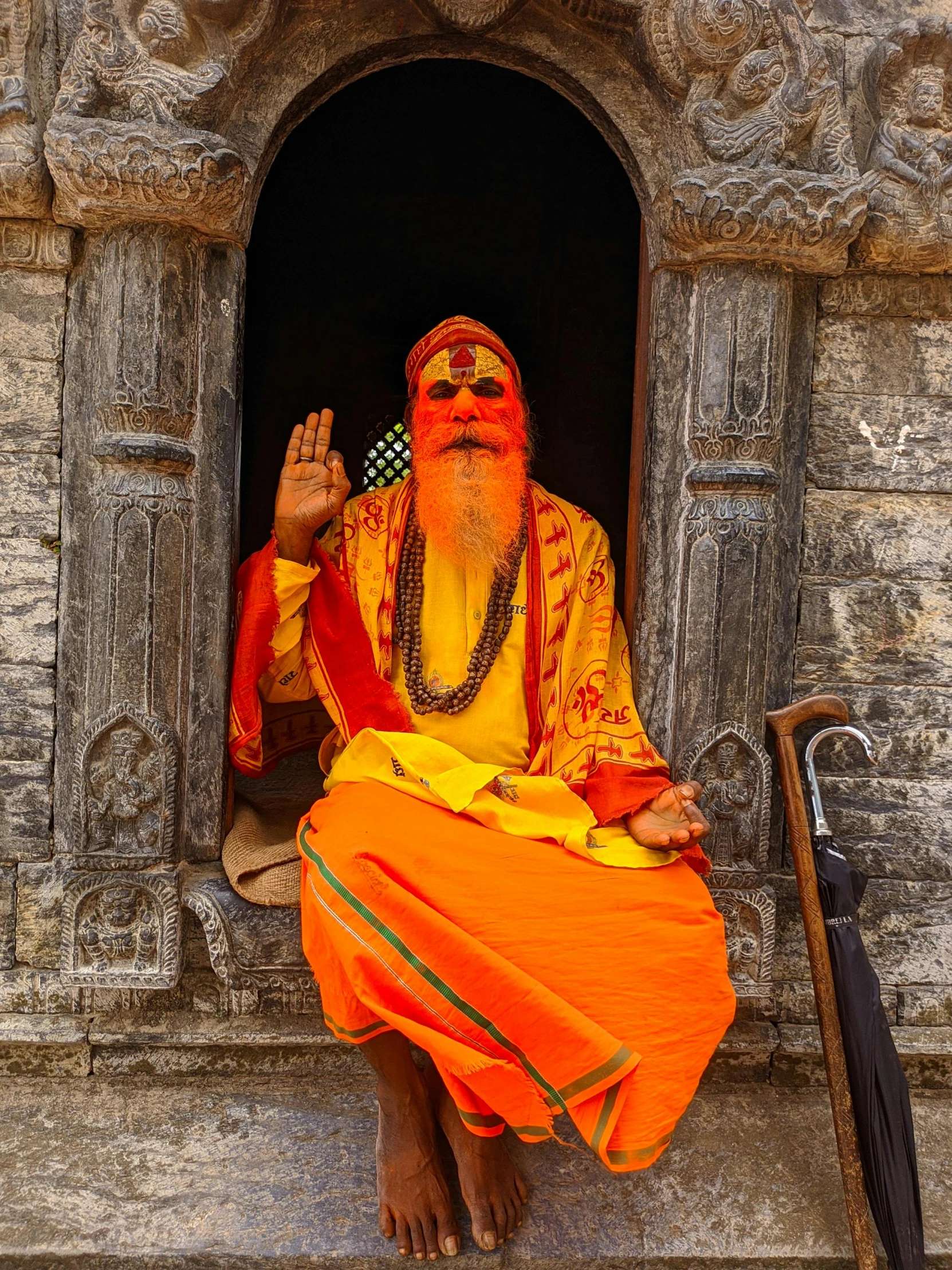 man with orange body and gold body and sunglasses sits on the window sill of a temple