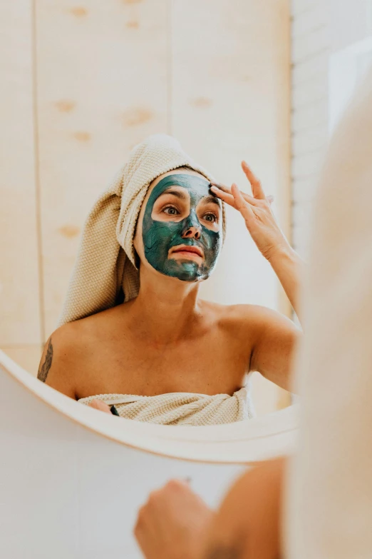 a woman is reflected in a mirror with a clay mask on