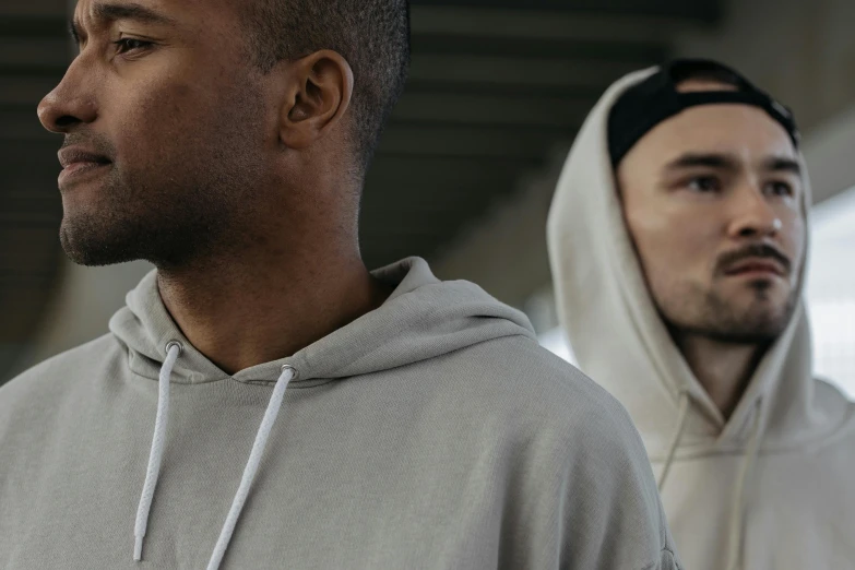 two men wearing hooded sweatshirts and one in black looking off to the side