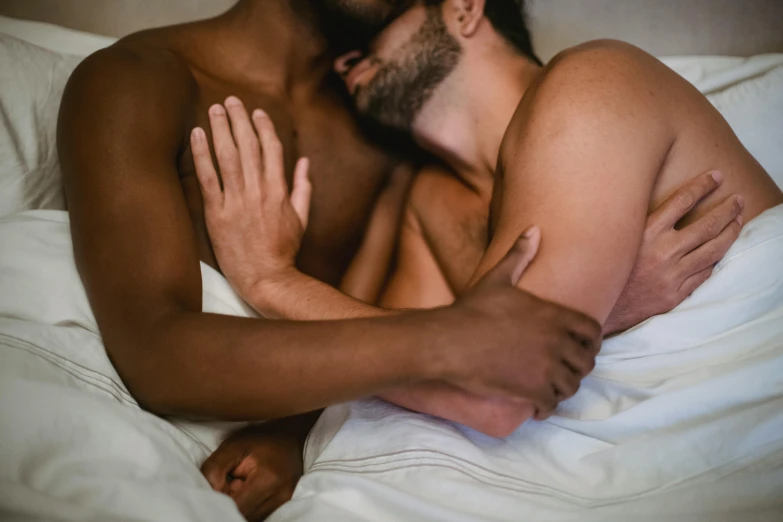 a shirtless man leaning against another shirtless man laying in bed