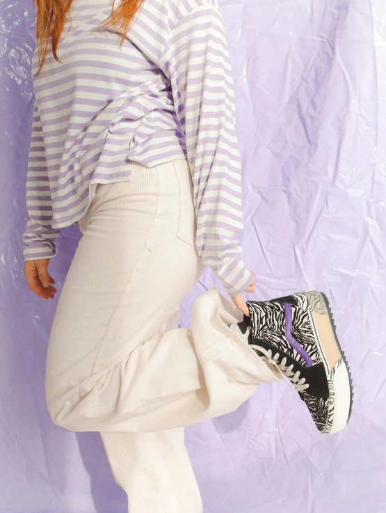 woman in white sweatpants posing against a purple backdrop