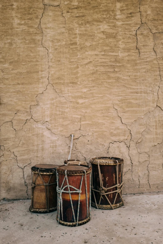 three old drum stands next to a tan wall