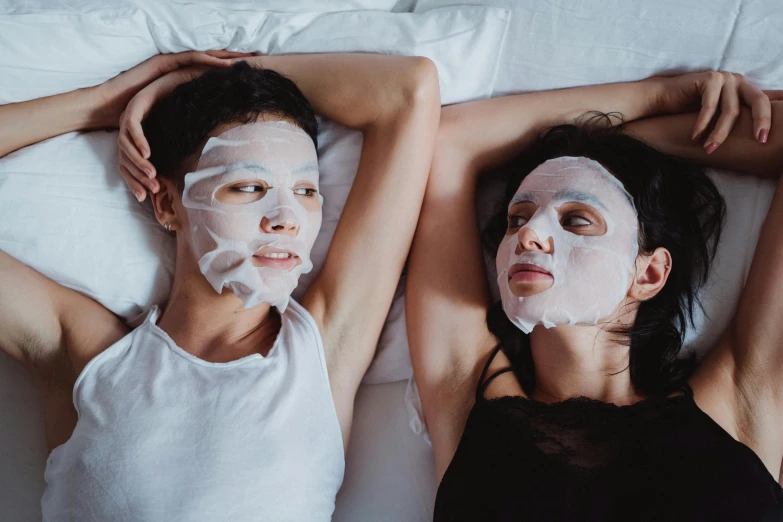 two girls laying on a bed with facial masks on