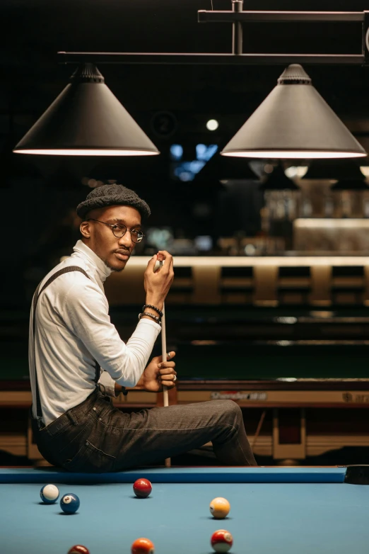 a man sitting on top of a pool table in front of lamps