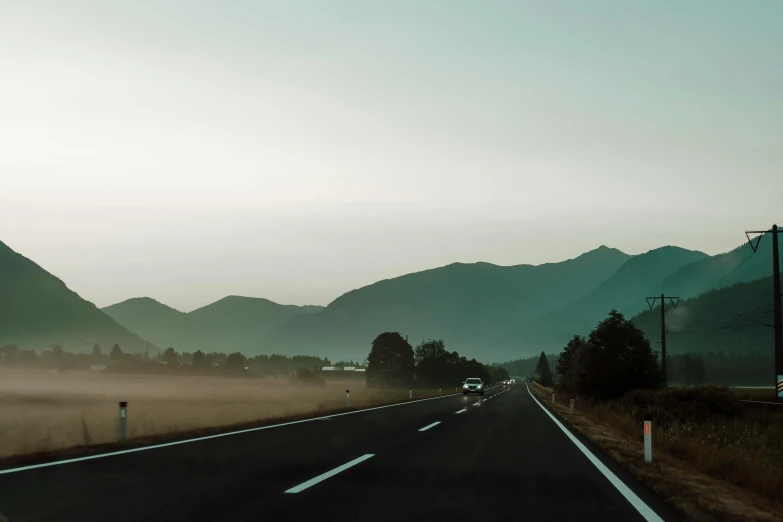 the sun is setting on a road with tall hills in the distance