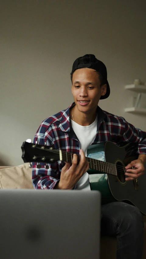 the young man is playing the guitar beside the laptop