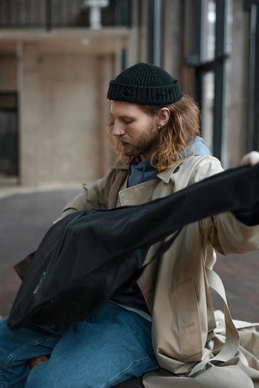 a man sits on top of a curb, playing with his handbag