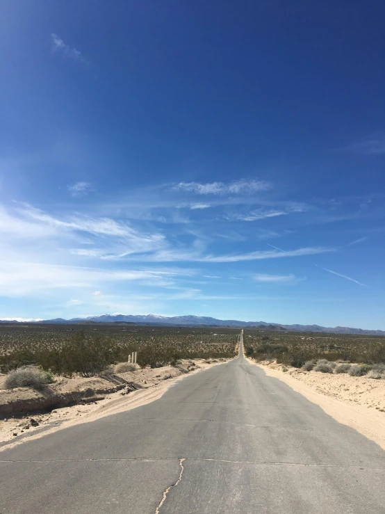 an empty open road in a desert, with mountains in the distance