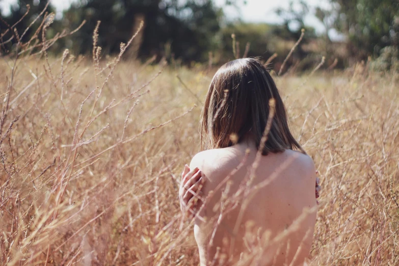 the topless woman stands  in the tall grass