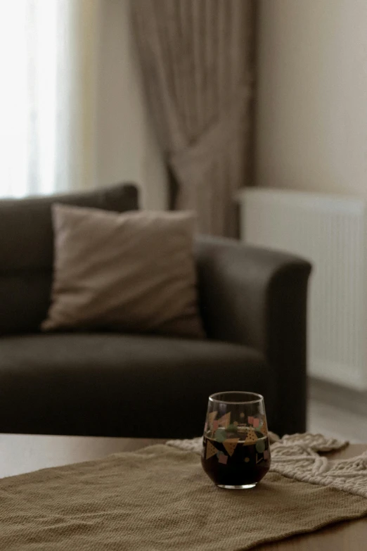 a living room area with a couch, window curtain and a glass on a table