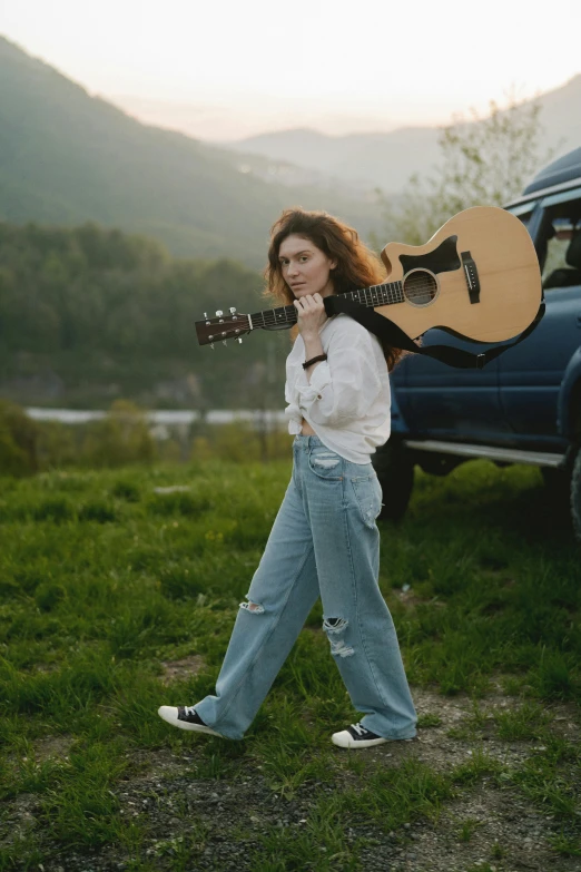 a woman with an acoustic guitar walking in the grass