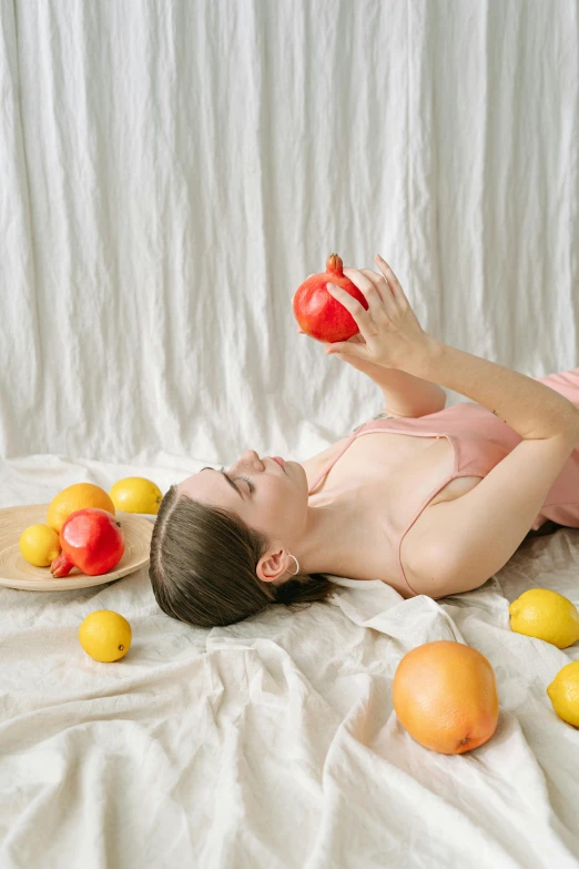 a woman laying down on the ground with apples and other fruits