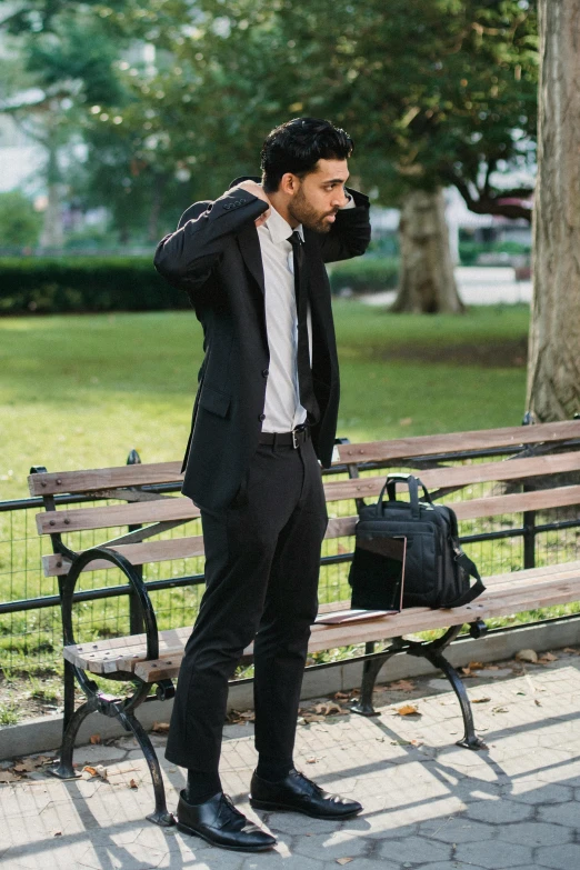 a man in suit and tie standing by a bench