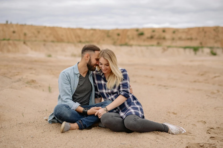 an engaged couple on the sand near grass