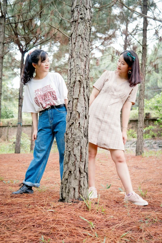 two teenage girls stand near a tree in a forest