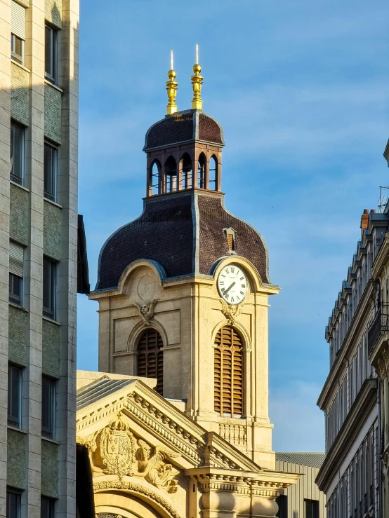 a large clock tower with the top of it sitting next to tall buildings