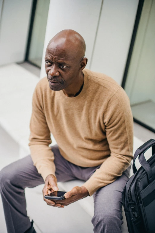 a black man sitting on top of a luggage bag looking at his phone