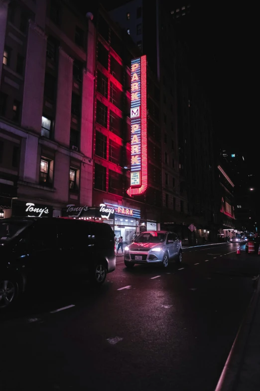 a night time scene shows cars driving along the road, with a lit building behind them